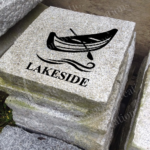 Engraved granite cottage accent stone feature with "Lakeside" and waves/canoe outside.