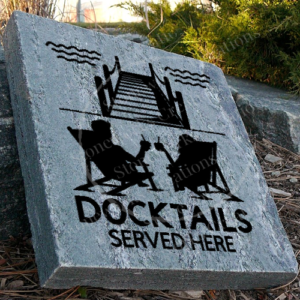 Engraved granite cottage/lake accent stone feature with "Docktails Served Here" and two people relaxing in chairs by dock having a drink near walkway.