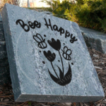 Engraved granite garden flower and bee accent stone with “Bee Happy” text displayed in garden /walkway setting.