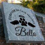 Engraved personalized granite pet memorial marker accent stone feature with "Forever In Our Hearts" and paw print, halo, wings near walkway.