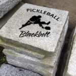 Engraved granite accent stone cottage garden feature with "Pickleball Blackbelt" and man in karate uniform holding paddle.