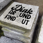 Engraved granite accent stone cottage garden feature with "Dink Around Find Out" and the "o" in "around"/"out" being replaced by pickleballs outside.