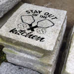 Engraved granite accent stone cottage or garden feature with "Mid-Life Crisis" and pickleball court/paddle/balls placed outside near walkway.