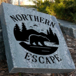 Engraved granite cottage stone with bear silhouette and trees design that says northern escape.