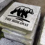 Engraved granite cottage stone with bear silhouette and trees design that says the hideaway.