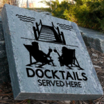 Engraved granite cottage stone with two people in chairs facing the dock with drinks design that says docktails served here.