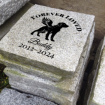 Engraved personalized granite pet memorial marker accent stone feature with "Forever Loved" and dog, wings near walkway.