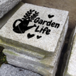 Engraved granite accent stone garden feature with "Garden Life" and flower pot/hearts near walkway.