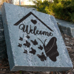 Engraved granite garden accent stone featuring rooftop, butterflies and heart with "Welcome" near walkway.